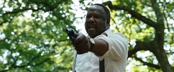 Movie still from “Cocaine Bear” (2023), directed by Elizabeth Banks – A man in a white shirt and tie holding a gun in his hand; Close Up shot, Low angle