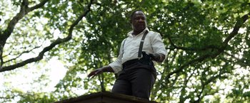 Movie still from “Cocaine Bear” (2023), directed by Elizabeth Banks – A man wearing suspenders standing on top of a building; Medium shot, Low angle