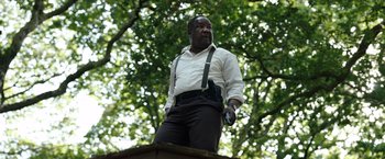 Movie still from “Cocaine Bear” (2023), directed by Elizabeth Banks – A man holding a cell phone while standing on top of a platform; Medium shot, Low angle