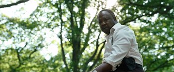 Movie still from “Cocaine Bear” (2023), directed by Elizabeth Banks – A man in a white shirt and tie standing in front of a tree; Close Up shot, Low angle