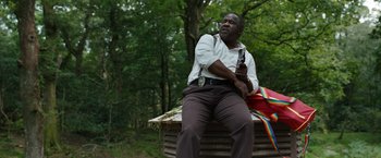 Movie still from “Cocaine Bear” (2023), directed by Elizabeth Banks – A man sitting on top of a bench holding a gun; Medium shot, Low angle