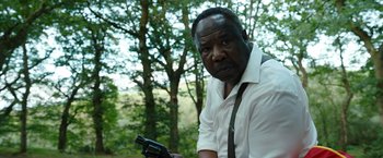 Movie still from “Cocaine Bear” (2023), directed by Elizabeth Banks – A man holding a gun while standing in front of trees; Close Up shot, Over the shoulder angle