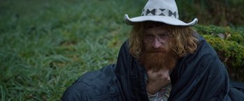 Movie still from “Cocaine Bear” (2023), directed by Elizabeth Banks – A man with long red hair and a beard wearing a white hat; Close Up shot, High angle