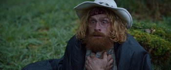 Movie still from “Cocaine Bear” (2023), directed by Elizabeth Banks – A man with long red hair and a beard wearing a cowboy hat; Close Up shot, Over the shoulder angle