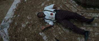 Movie still from “Cocaine Bear” (2023), directed by Elizabeth Banks – A man with blood on his shirt lies on the ground; Medium shot, Overhead angle