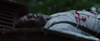 Movie still from “Cocaine Bear” (2023), directed by Elizabeth Banks – A man laying on the ground with a knife in his mouth; Close Up shot, Low angle