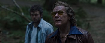 Movie still from “Cocaine Bear” (2023), directed by Elizabeth Banks – A man wearing sunglasses standing next to another man in a forest; Close Up shot, Over the shoulder angle