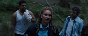 Movie still from “Cocaine Bear” (2023), directed by Elizabeth Banks – A woman with dreads standing next to a tree; Medium shot, Over the shoulder angle