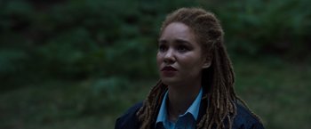 Movie still from “Cocaine Bear” (2023), directed by Elizabeth Banks – A woman with dreads standing in the woods; Close Up shot, Low angle
