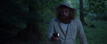 Movie still from “Cocaine Bear” (2023), directed by Elizabeth Banks – A man with a beard holding a cell phone; Medium shot, Over the shoulder angle