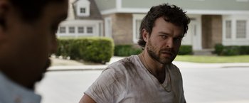 Movie still from “Cocaine Bear” (2023), directed by Elizabeth Banks – A person wearing a white shirt near a house; Close Up shot, Low angle