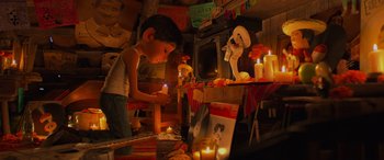 Movie still from “Coco” (2017), directed by Adrian Molina – A boy lighting a candle in front of an animated character; Wide shot, High angle