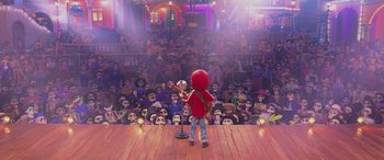 Movie still from “Coco” (2017), directed by Adrian Molina – A person in a red shirt is playing a guitar in front of a crowd; Wide shot, Over the shoulder angle