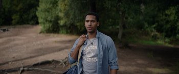 Movie still from “Color Out of Space” (2019), directed by Richard Stanley – A young man holding a blue bag in a wooded area; Medium shot, Over the shoulder angle