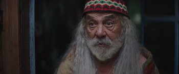 Movie still from “Color Out of Space” (2019), directed by Richard Stanley – An old man with long white beard wearing a colorful hat; Close Up shot, Over the shoulder angle
