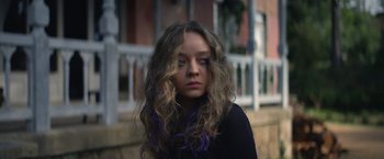Movie still from “Color Out of Space” (2019), directed by Richard Stanley – A woman with purple hair standing in front of a building; Close Up shot, Over the shoulder angle