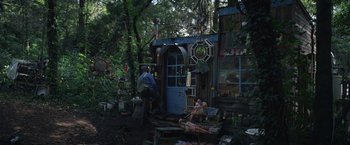 Movie still from “Color Out of Space” (2019), directed by Richard Stanley – A man and a woman sitting in front of a house in the woods; Wide shot, Low angle