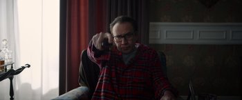 Movie still from “Color Out of Space” (2019), directed by Richard Stanley – A man sitting on a couch holding a remote control; Medium shot, Over the shoulder angle