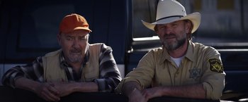 Movie still from “Color Out of Space” (2019), directed by Richard Stanley – A couple of men sitting next to each other on a bench; Medium shot, Low angle