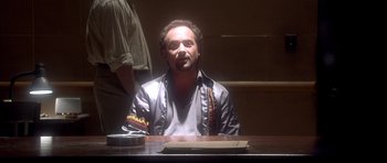 Movie still from “The Usual Suspects” (1995), directed by Bryan Singer – A man sitting at a table in front of a window; Medium shot, Low angle
