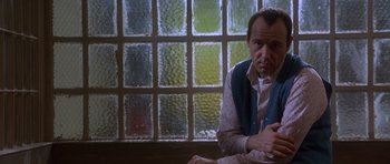 Movie still from “The Usual Suspects” (1995), directed by Bryan Singer – A man sitting in front of a glass window; Close Up shot, Low angle