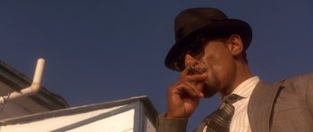Movie still from “The Usual Suspects” (1995), directed by Bryan Singer – A man wearing a hat and sunglasses talking on a cell phone; Close Up shot, Low angle