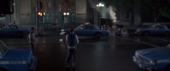 Movie still from “The Usual Suspects” (1995), directed by Bryan Singer – A man standing in the middle of a street next to a blue car; Wide shot, High angle