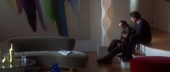 Movie still from “The Usual Suspects” (1995), directed by Bryan Singer – A man sitting on a chair next to a painting; Wide shot, High angle