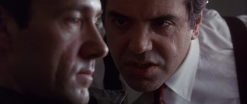 Movie still from “The Usual Suspects” (1995), directed by Bryan Singer – A man in a suit and tie looking at another man in a suit and tie; Close Up shot, Over the shoulder angle