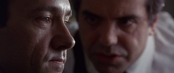 Movie still from “The Usual Suspects” (1995), directed by Bryan Singer – A man looking at another man in a dark room; Extreme Close Up shot, Low angle