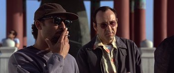 Movie still from “The Usual Suspects” (1995), directed by Bryan Singer – A man smoking a cigarette next to another man wearing sunglasses; Close Up shot, Low angle