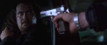Movie still from “The Usual Suspects” (1995), directed by Bryan Singer – A man holding a gun in front of a car window; Close Up shot, Low angle