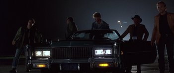 Movie still from “The Usual Suspects” (1995), directed by Bryan Singer – A couple of people standing on the hood of a car at night; Wide shot, Low angle