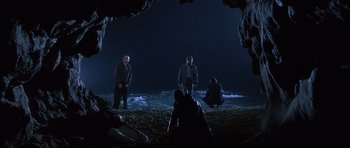 Movie still from “The Usual Suspects” (1995), directed by Bryan Singer – A group of people standing on top of a sandy beach at night; Wide shot, High angle