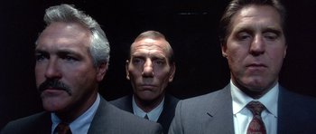Movie still from “The Usual Suspects” (1995), directed by Bryan Singer – A man in a suit and tie standing next to two other men; Close Up shot, Low angle