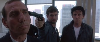 Movie still from “The Usual Suspects” (1995), directed by Bryan Singer – A man holding a gun while standing next to two other men; Close Up shot, Low angle