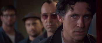 Movie still from “The Usual Suspects” (1995), directed by Bryan Singer – A person wearing a hat and sunglasses; Close Up shot, Over the shoulder angle
