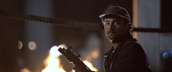 Movie still from “The Usual Suspects” (1995), directed by Bryan Singer – A man holding a gun while standing in front of a fire pit; Close Up shot, Low angle