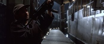 Movie still from “The Usual Suspects” (1995), directed by Bryan Singer – A person holding a gun while standing on a train platform; Medium shot, Low angle
