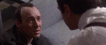 Movie still from “The Usual Suspects” (1995), directed by Bryan Singer – A man sitting on a couch talking to another man; Close Up shot, Over the shoulder angle