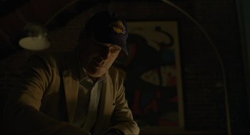 Movie still from “Confess, Fletch” (2022), directed by Greg Mottola – A man wearing a baseball cap is reading a book; Close Up shot, Over the shoulder angle