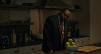 Movie still from “Confess, Fletch” (2022), directed by Greg Mottola – A man standing in a kitchen next to a bowl of fruit; Medium shot, Over the shoulder angle