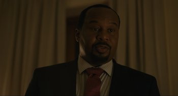 Movie still from “Confess, Fletch” (2022), directed by Greg Mottola – A man wearing a suit and tie in front of a window; Close Up shot, Over the shoulder angle