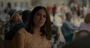 Movie still from “Confess, Fletch” (2022), directed by Greg Mottola – A beautiful young lady wearing a tan top; Close Up shot, Over the shoulder angle