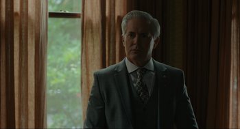 Movie still from “Confess, Fletch” (2022), directed by Greg Mottola – A man in a suit and tie standing in front of a window; Close Up shot, Low angle