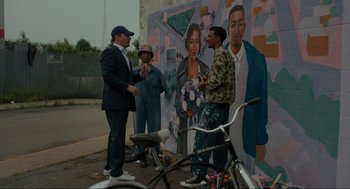 Movie still from “Confess, Fletch” (2022), directed by Greg Mottola – A group of people standing in front of a mural; Medium shot, Over the shoulder angle