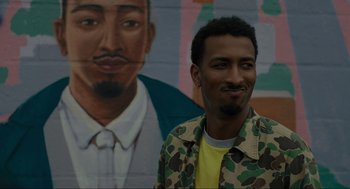 Movie still from “Confess, Fletch” (2022), directed by Greg Mottola – A man standing in front of a painting of a man; Close Up shot, Over the shoulder angle