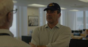 Movie still from “Confess, Fletch” (2022), directed by Greg Mottola – A man wearing a baseball cap and a striped shirt; Medium shot, Over the shoulder angle