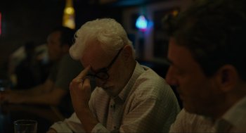 Movie still from “Confess, Fletch” (2022), directed by Greg Mottola – An older man sitting in front of a group of people; Close Up shot, Over the shoulder angle