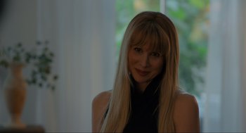 Movie still from “Confess, Fletch” (2022), directed by Greg Mottola – A woman with long blonde hair wearing a black top; Close Up shot, Over the shoulder angle